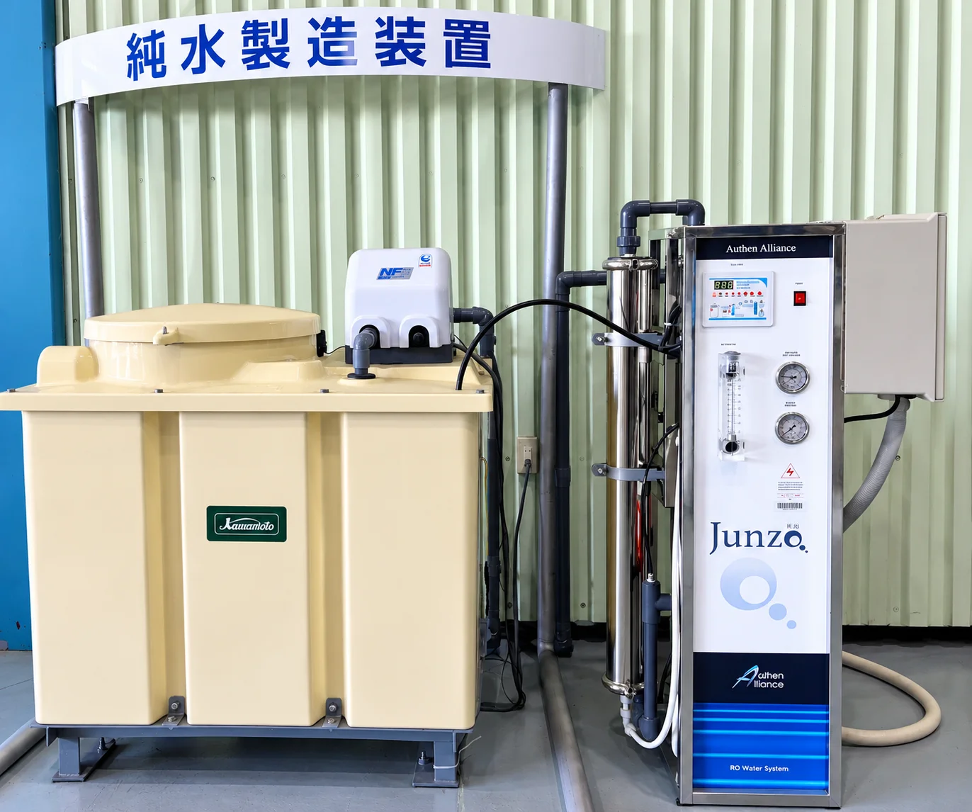 「純水製造装置」と表示された看板、Kawamoto製ポンプを備えたベージュ色の大型純水タンク、流量計・圧力計・純度表示パネルが並ぶステンレス製RO装置本体で構成された、屋内に設置済みのRO式純水製造装置の全景